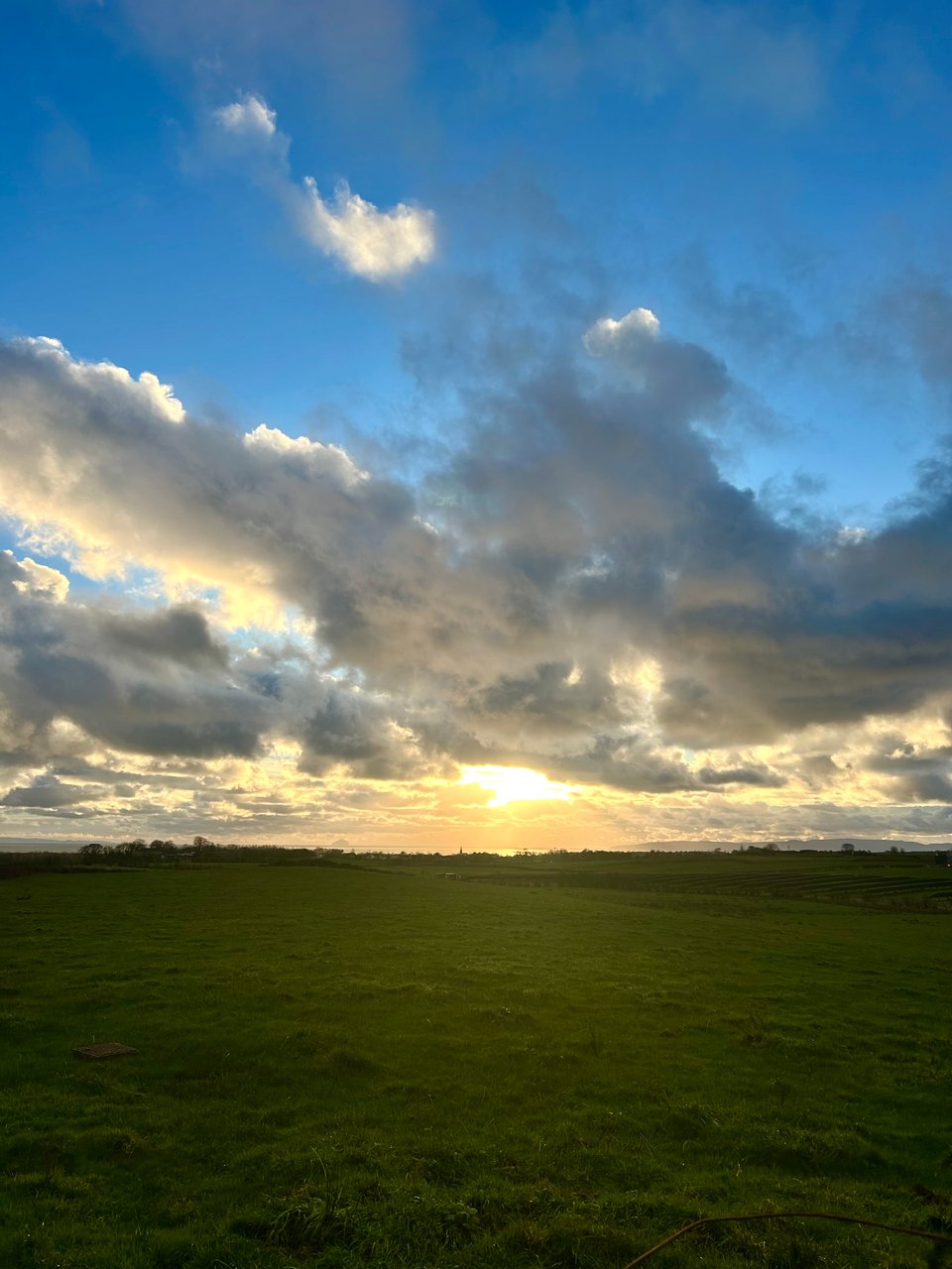 Golden sun is breaking through thick grey clouds and shining over the distant sea and islands in south west Scotland. Image by Rowan Ambrose.