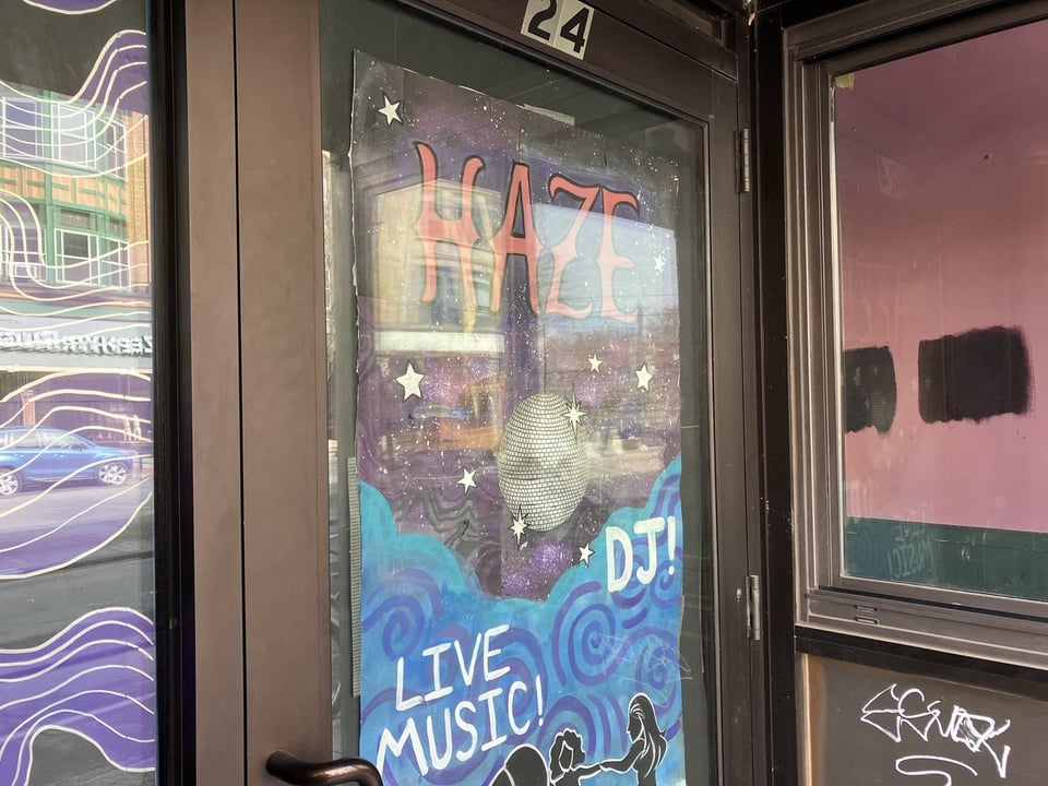 A glass door cover over with a sheet of paper that reads "HAZE" and depicts a disco ball with the words "Live Music!" and "DJ!" in white against a blue background