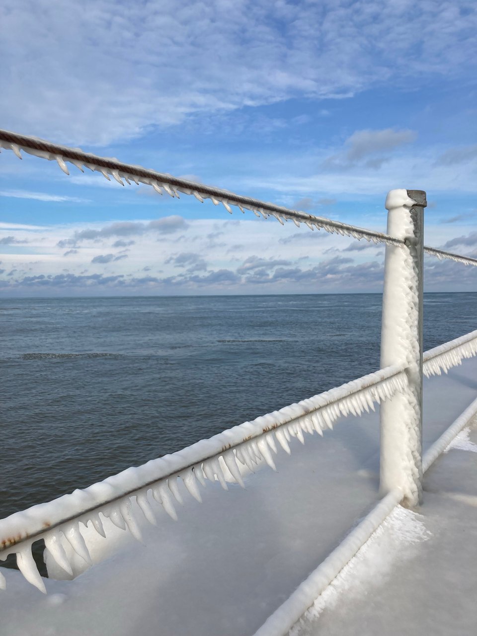 a railing on a Lake Ontario pier, coated in snow that wind has shaped into icicles.