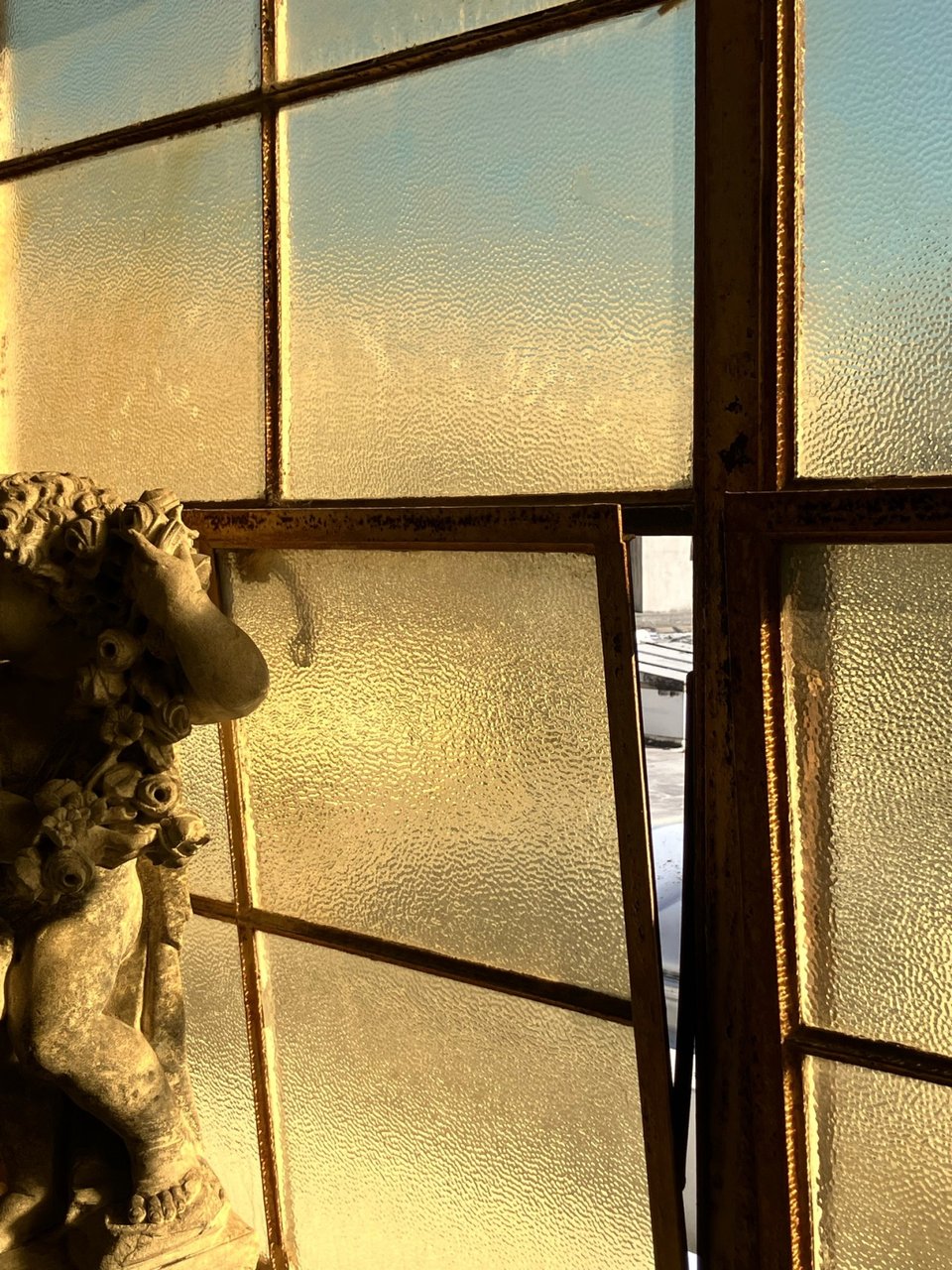 A window cracked open, revealing a slice of pale concrete in contrast to the golden panes.