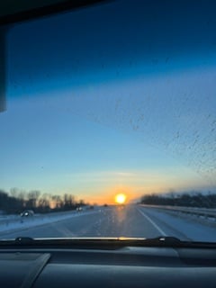 windshield view of orange sun on the horizon under a blue sky