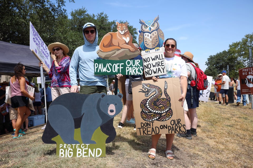 Parks enthusiasts hold signs advocating for state parkland protection from border infrastructure.