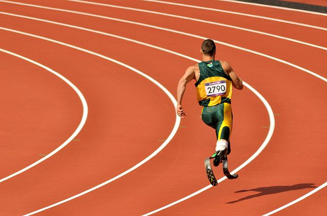 A man with two prosthetic legs, runs on the track. We're seeing him from behind.