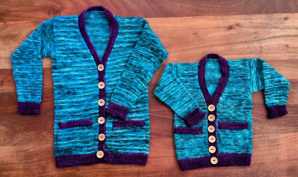 Two matching children's sized button-up cardigans (one for a four-year-old, one for a baby) in a variegated turquoise color with deep purple accents on the pockets, hem, button band, and cuffs.