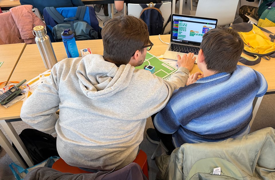 A man and a boy sit at a table and work on programming a robotic cube to play football using the language "SNAP".
