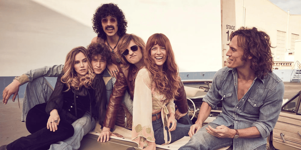 A rock band sitting in a convertible, smiling at the camera.