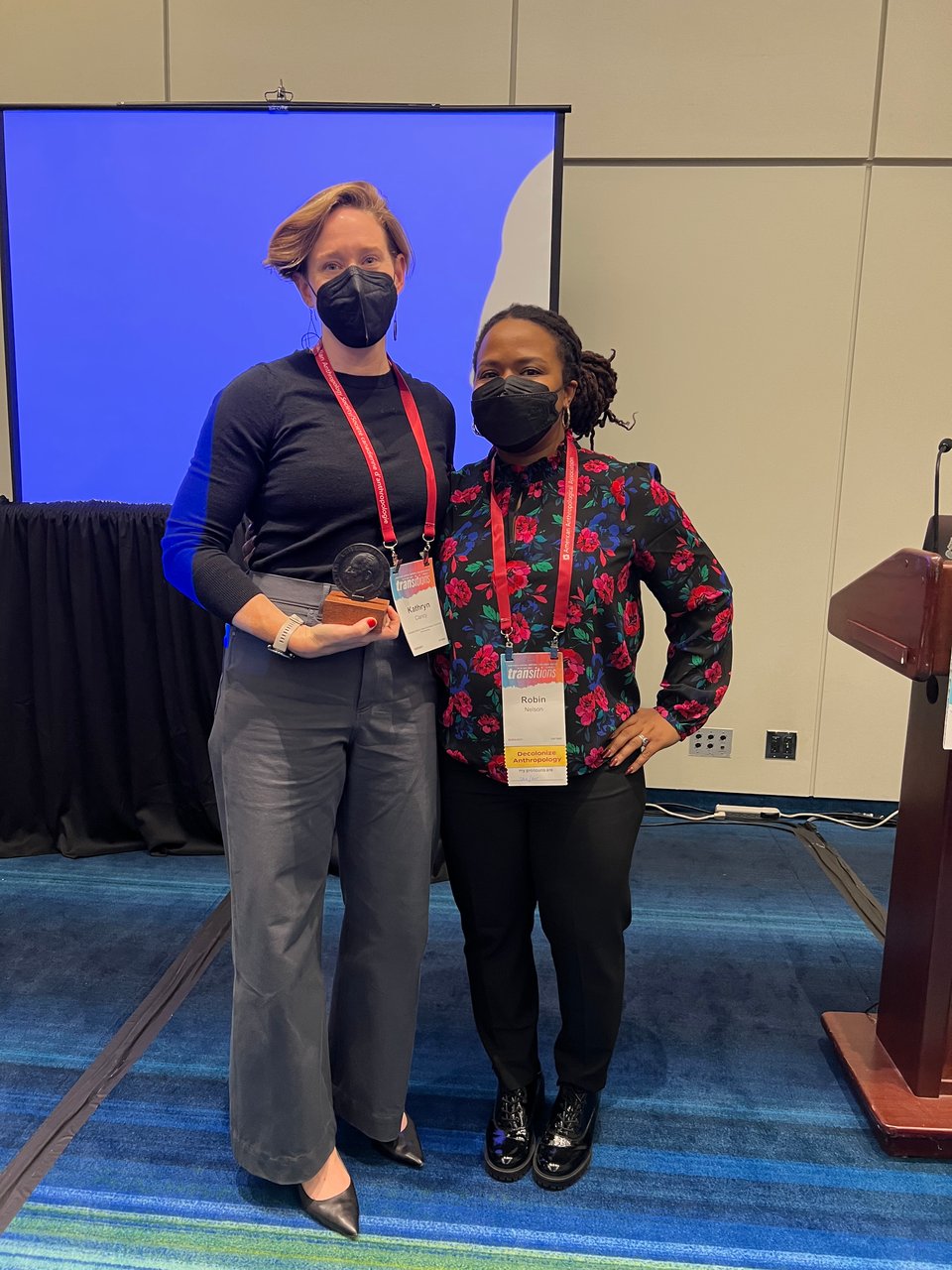 Photograph of Kate Clancy and Robin Nelson, both wearing masks. Kate is holding her book award.