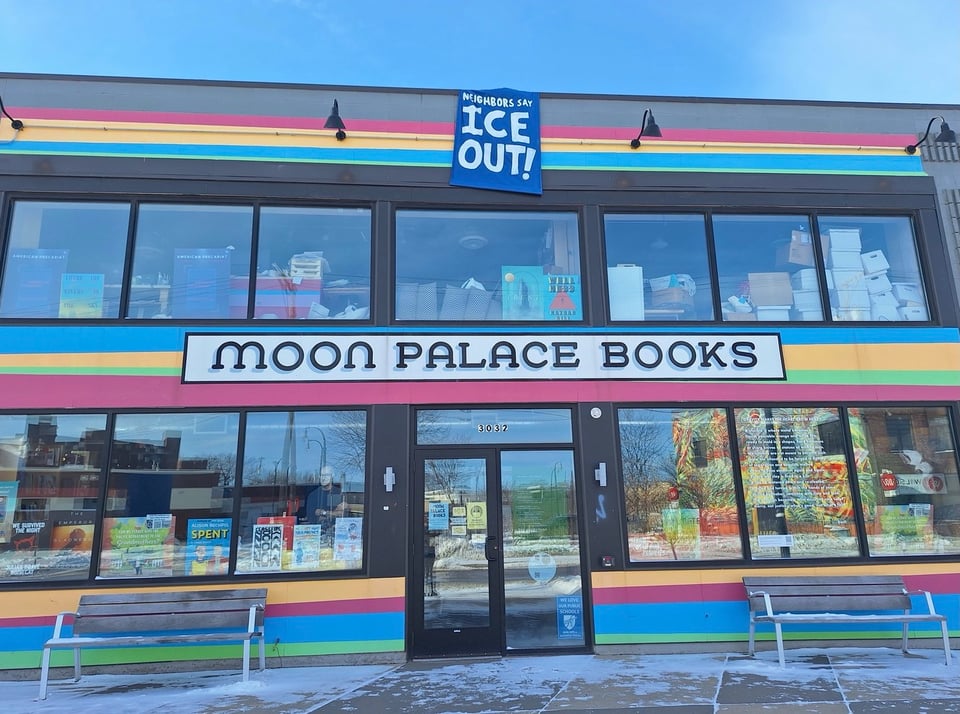 A photograph of Moon Palace Books, a bookstore painted with a rainbow facade. A banner reading "ICE OUT!" hangs over the front door.