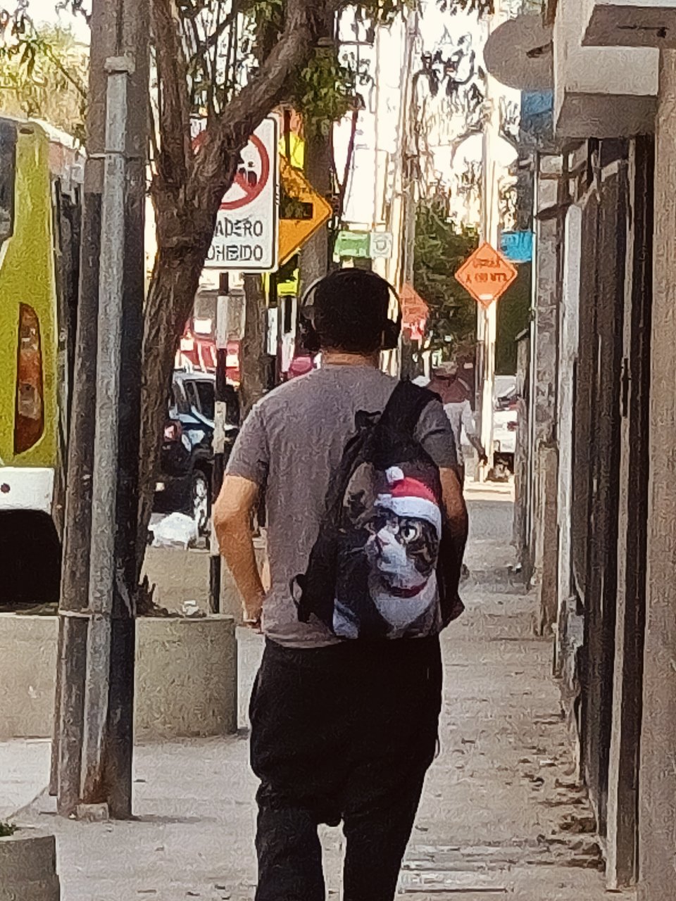 A man walking down a Lima street wearing a rucksack with a funny picture of a cat wearing a santa hat