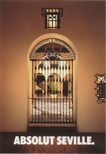 Absolut vodka advertisement. The headline is ABSOLUT SEVILLE. The image is a classic Seville courtyard viewed through an arched gateway in the shape of the Absolut bottle.