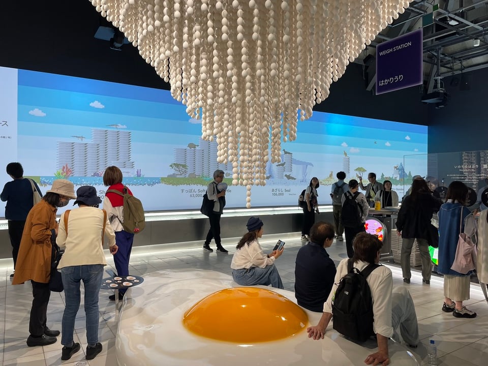 A waterfall chandelier of eggs dangles from the ceiling above a massive sunny side up egg that is a seated resting spot for viewers of the Earth Mart exhibit.