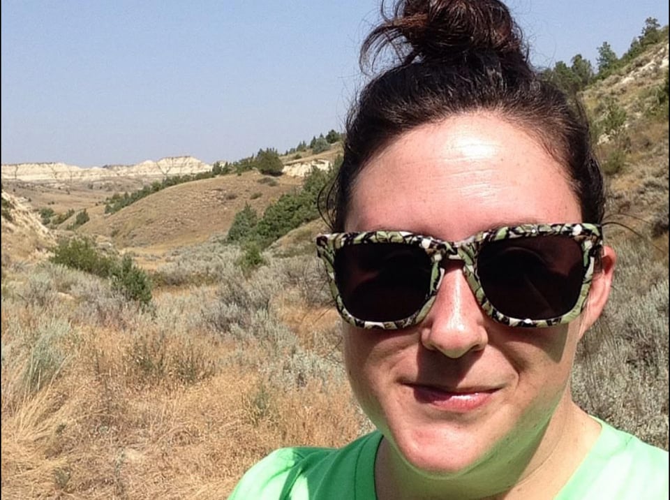 Selfie on the Maah Daah Hey Trail in 2019. I'm wearing very cool glasses, a lime green tee, and have a bad hair bun.