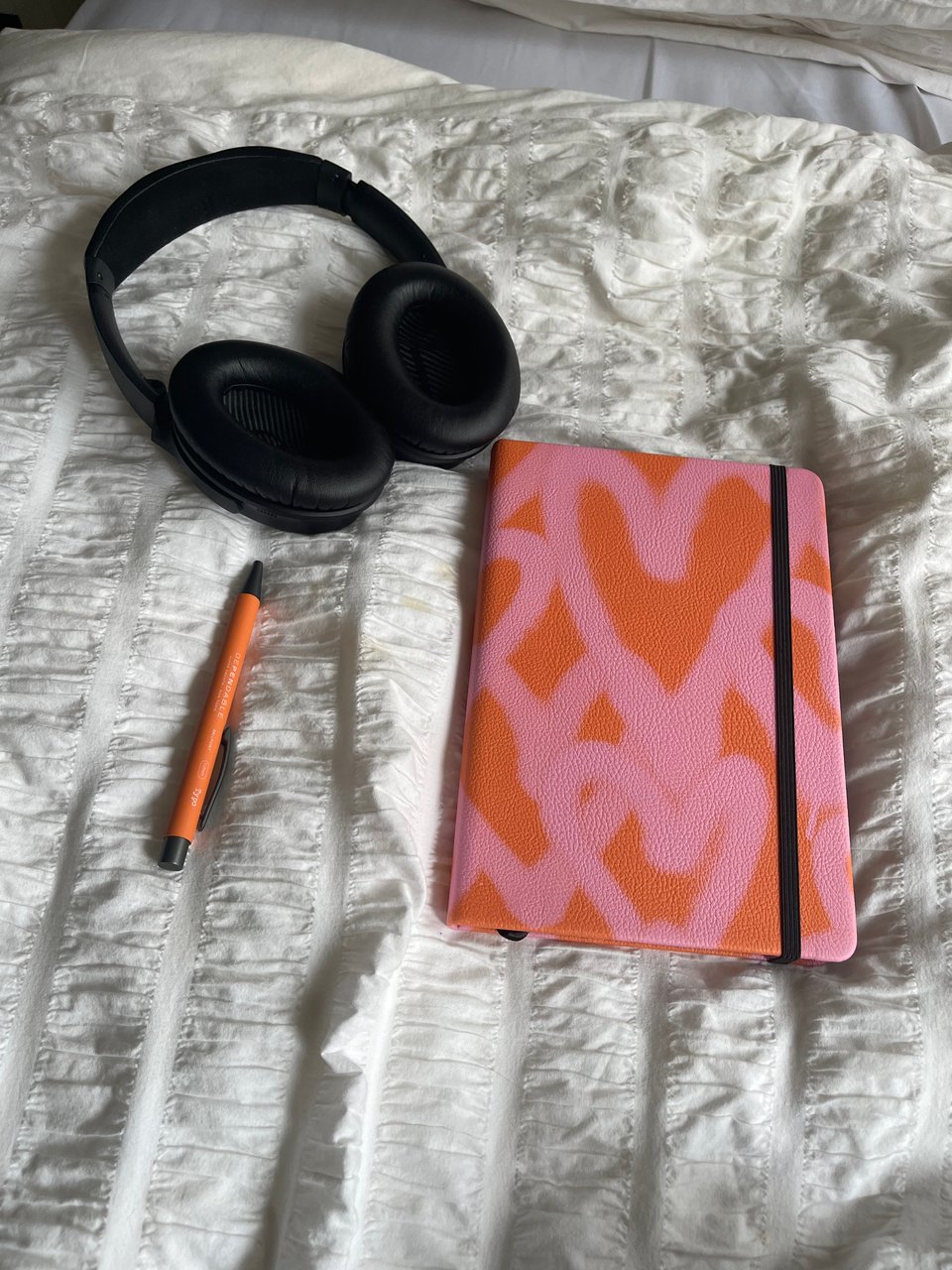 Stock photo of a pair of headphones, a pen, and a notebook on a bed.