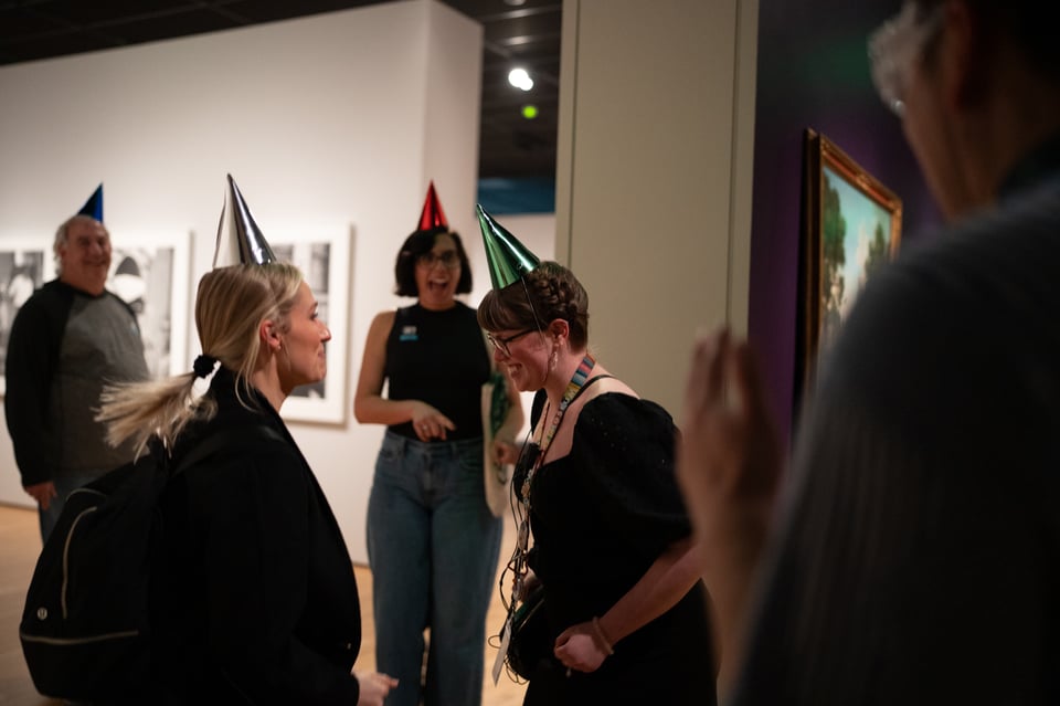 A group of people wearing birthday hats in a gallery.