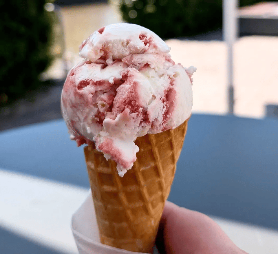 A close up of an ice cream cone with white vanilla ice cream with red raspberry jam stripes