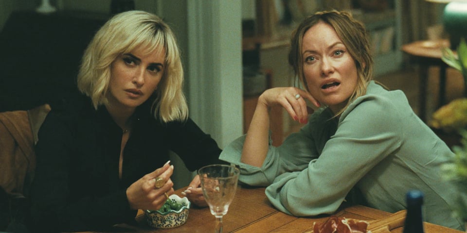 Olivia Wilde and Penelope Cruz sit at a table and look aghast.