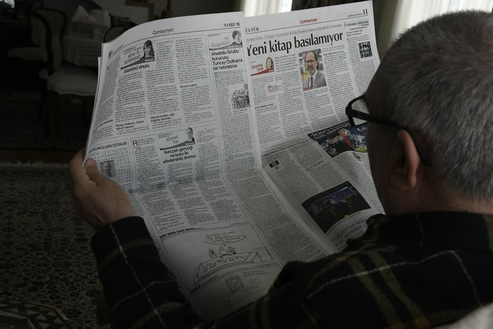 A man sitting at a table, reading a newspaper. Photo by Anna Keibalo on Unsplash.