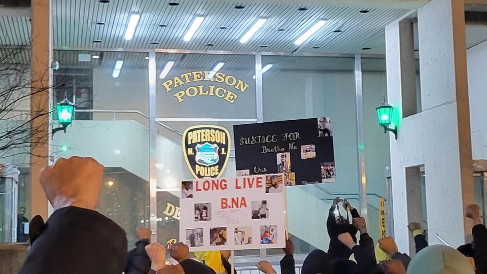 Protestors March to the front of the Paterson Police Department after officers had murdered Najee Seabrooks. Next to the Paterson Police Department signage are protest signs for Long Live B. Na and Justice for Brother Na.
