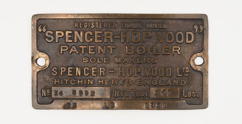Metal plate in width rectangular form, brass hued, with screw holes on left and right. Text reads: REGISTERED TRADE MARK "SPENCER-HOPWOOD" PATENT BOILER, SOLE MAKERS, SPENCER - HOPWOOD LTD, HITCHIN HERTS ENGLAND with a nubmer stamp and a weight limited expressed.