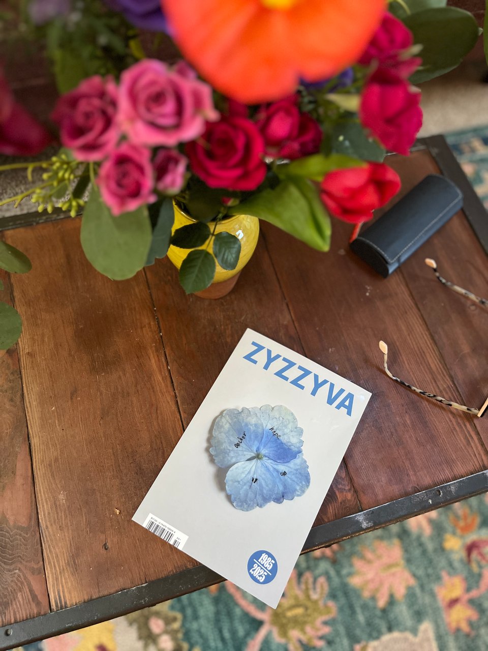 ZYZZYVA literary magazine on a wooden coffee table, beneath a large bouquet of pink and red tea roses