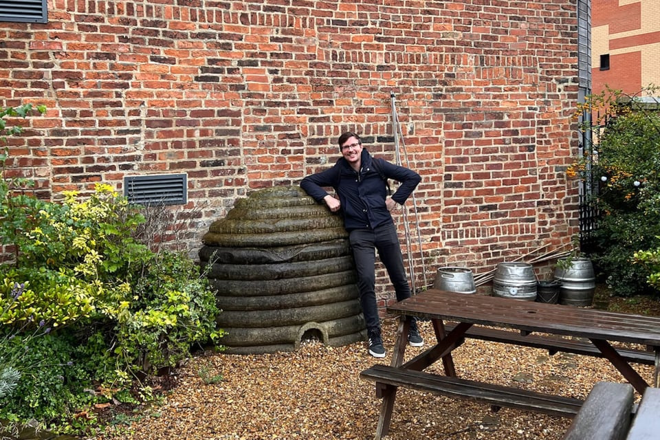 alt="A smiling dude posing next to a giant beehive ornament made out of stone"