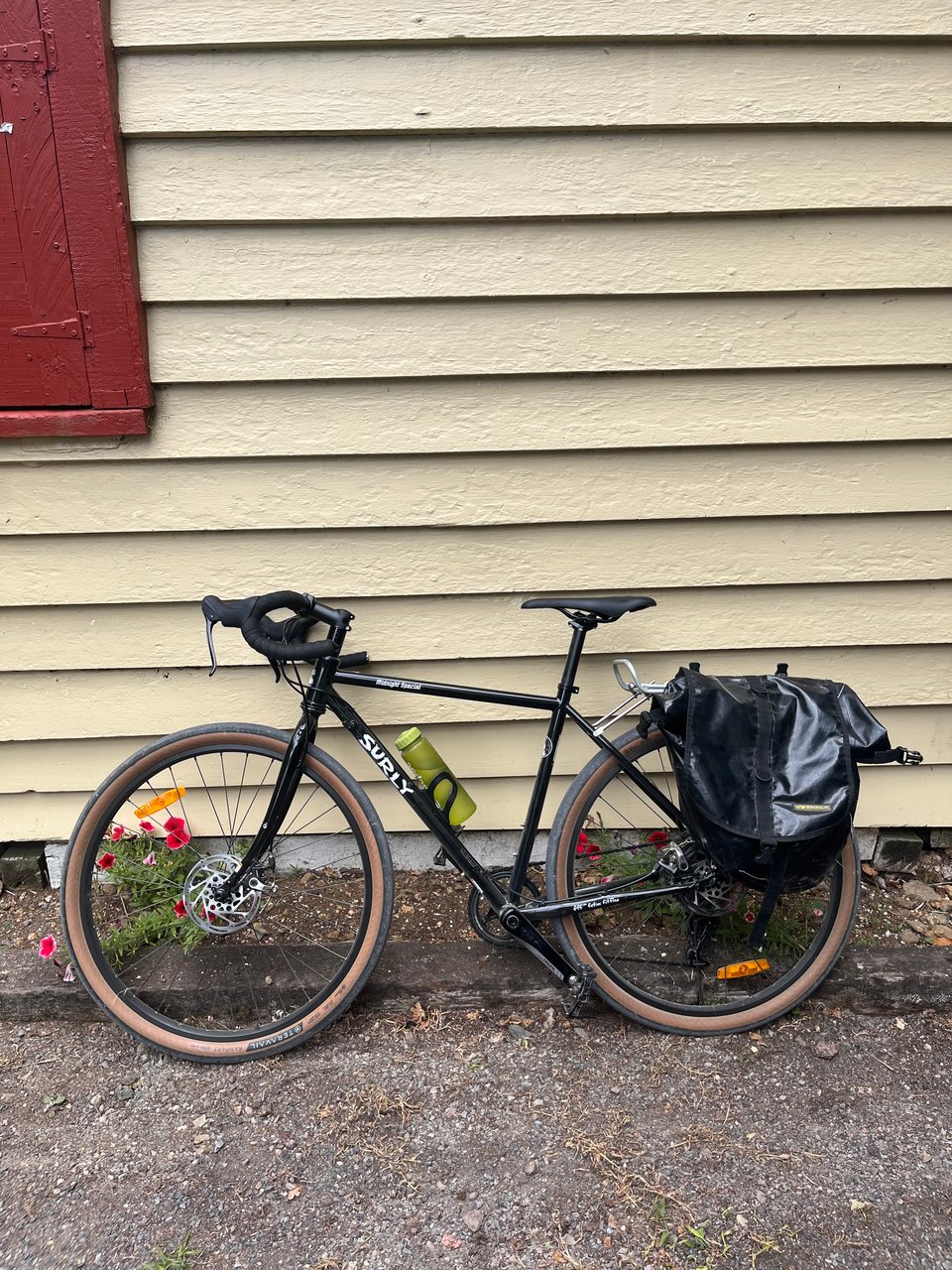 A photo of a black Surly road bike with thin frame rubes, tan tyre walls, and a black pannier on the back.