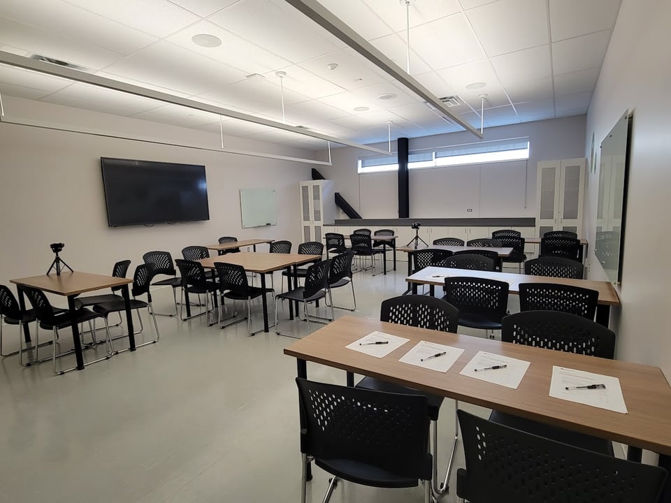A classroom set up with chairs and tables, with cameras pointing at some of them, and papers with pens ready for signing waivers.