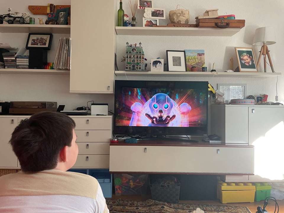A young boy looks at the large TV screen which shows a scene from "Wild Robot" where the robot looks at a duckling in its hand.
