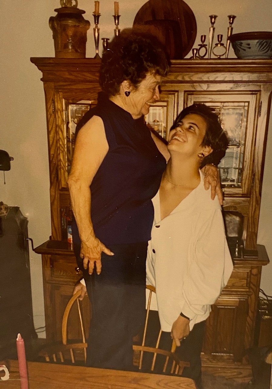 A small woman standing on a chair and smiling down at a woman who is smiling up at her