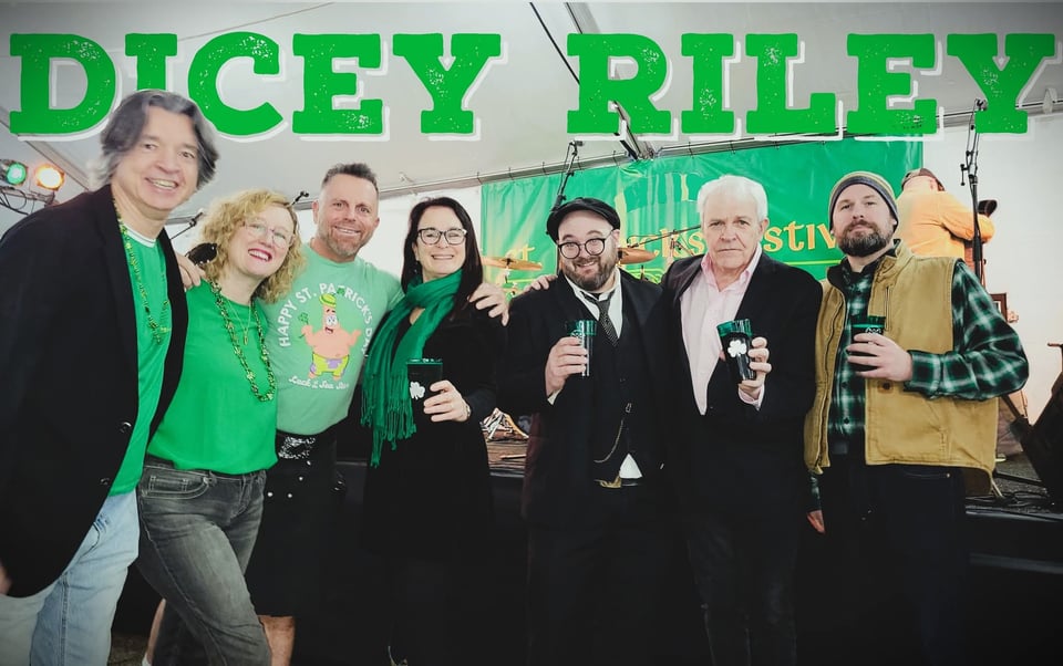 The Celtic-rock band Dicey Riley, featuring five men and two women standing shoulder to shoulder and smiling.
