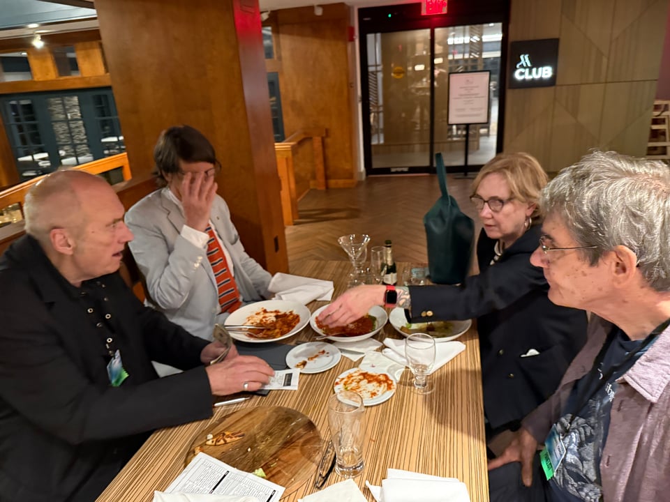 photo of four people at a wooden table in a hotel restaurant, trying to figure out the dinner check & the tip