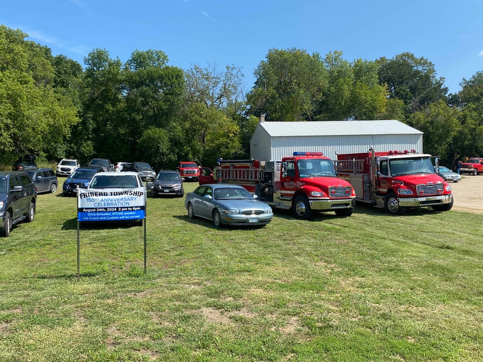 a friberg township banner in front of cars and two fire trucks to celebrate the 150th anniversary of incorporation