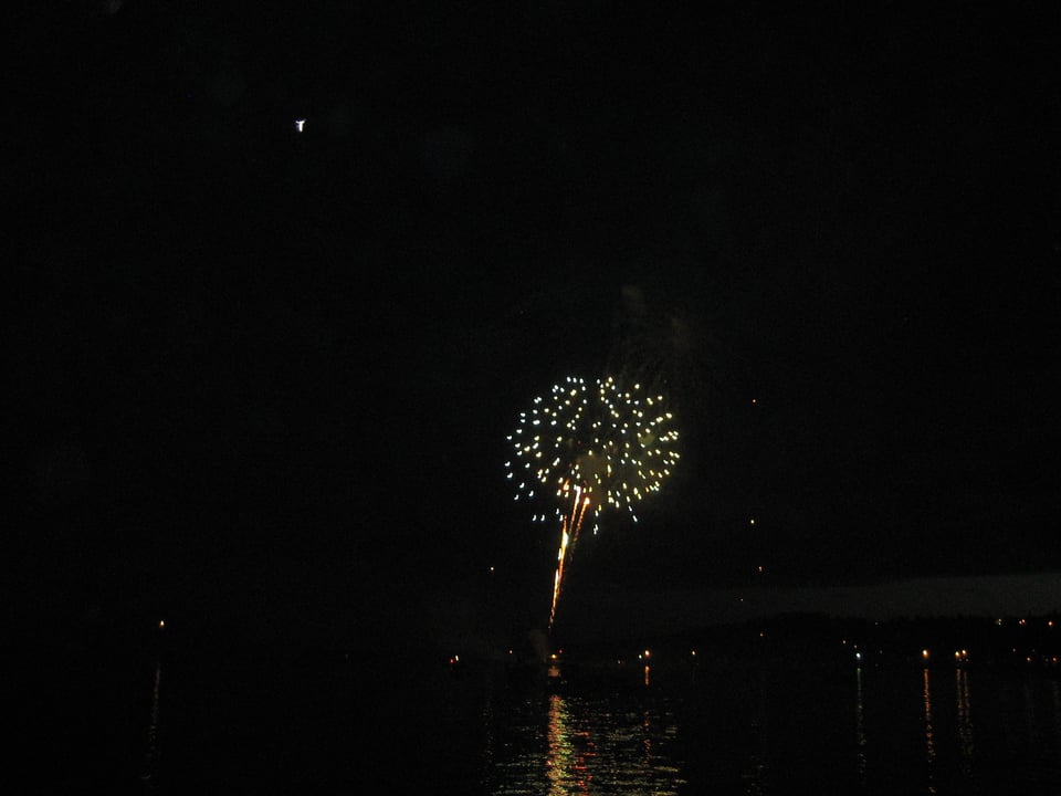 A burst of yellow-white fireworks reflected in water.