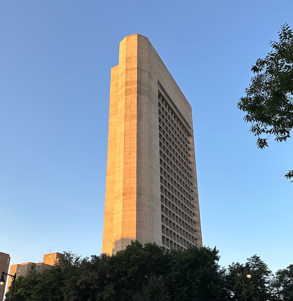 Photo of a brutalist skyscraper lit by morning sun against a blue sky