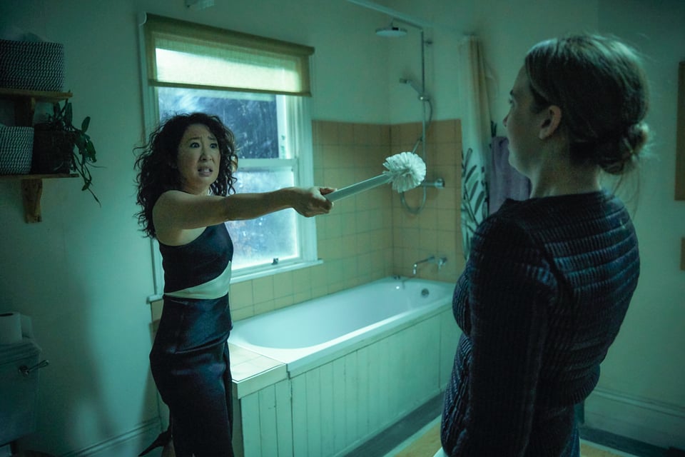 Publicity still of Eve wearing a tight black designer dress and confronting Villanelle with a toilet brush in her bathroom