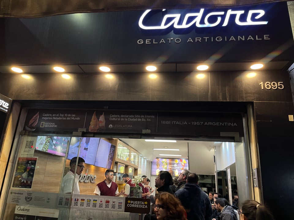 Entryway for 'Cadore' a world-famous ice cream store in Buenos Aires. It is full with customers waiting to pick up their orders and a line of people waiting outside to order