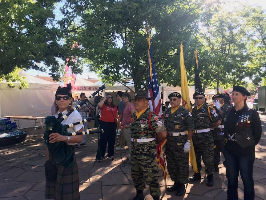 bagpiper waiting for the presentation of the flags to begin. behind her are uniformed veterans carrying flags of US and New Mexico.