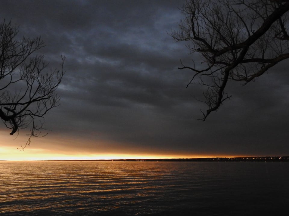 Extremely dark clouds over a lake, with a very bright line of sunlight farther down the lake.