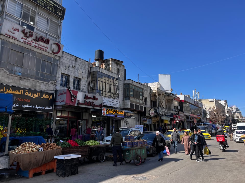 A street including stores with signs in Arabic under a bright blue sky
