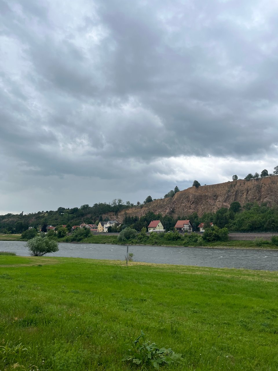 A broad river with green grassy banks, and a few houses beside.
