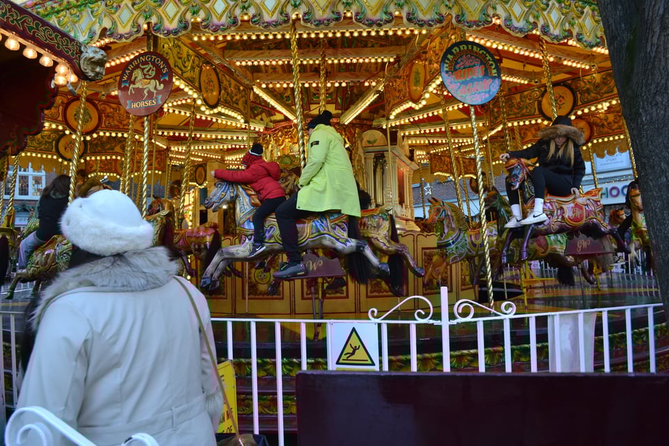 An old Victorian carousel, in motion, with various people riding.
