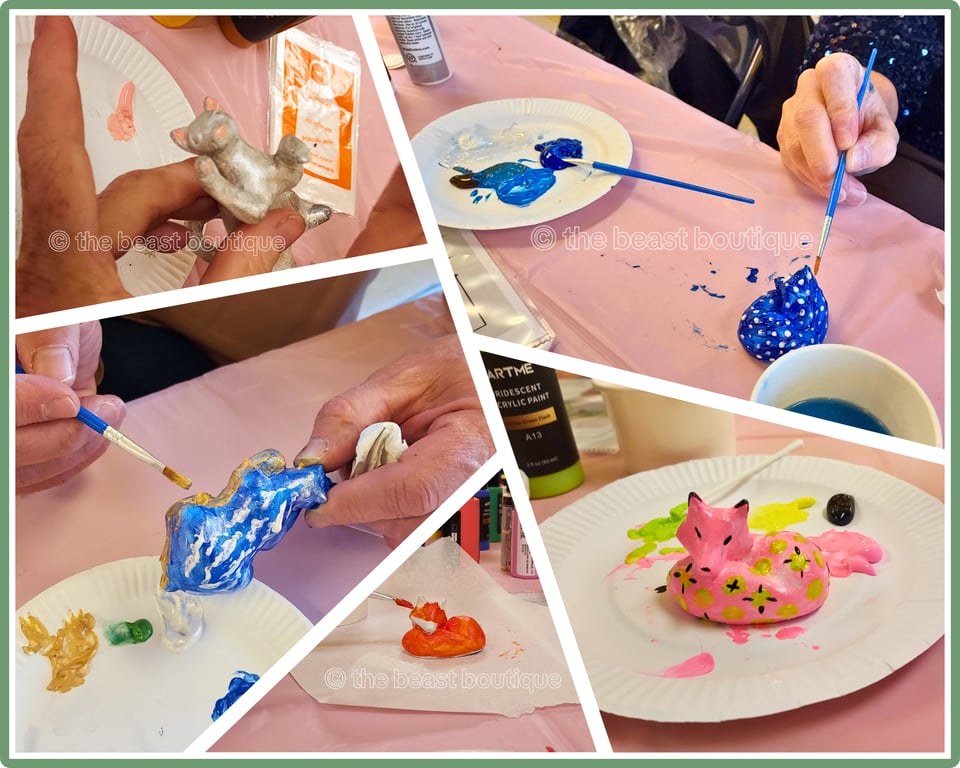 A collage of figurines being painted - top to bottom, left to right: A silver cat with a pink muzzle, a blue fox with white spots, a blue bear painted with clouds and a landscape, a red fox, and a pink fox with green spots and black details in the spots.
the shop name, the beast boutique, watermarks the image.