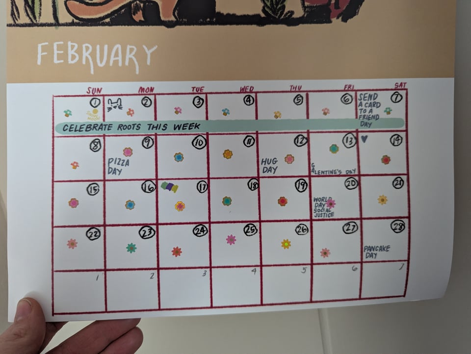 A hand holding a calendar page labeled "February." A tiny flower or mushroom sticker is in each day's box.