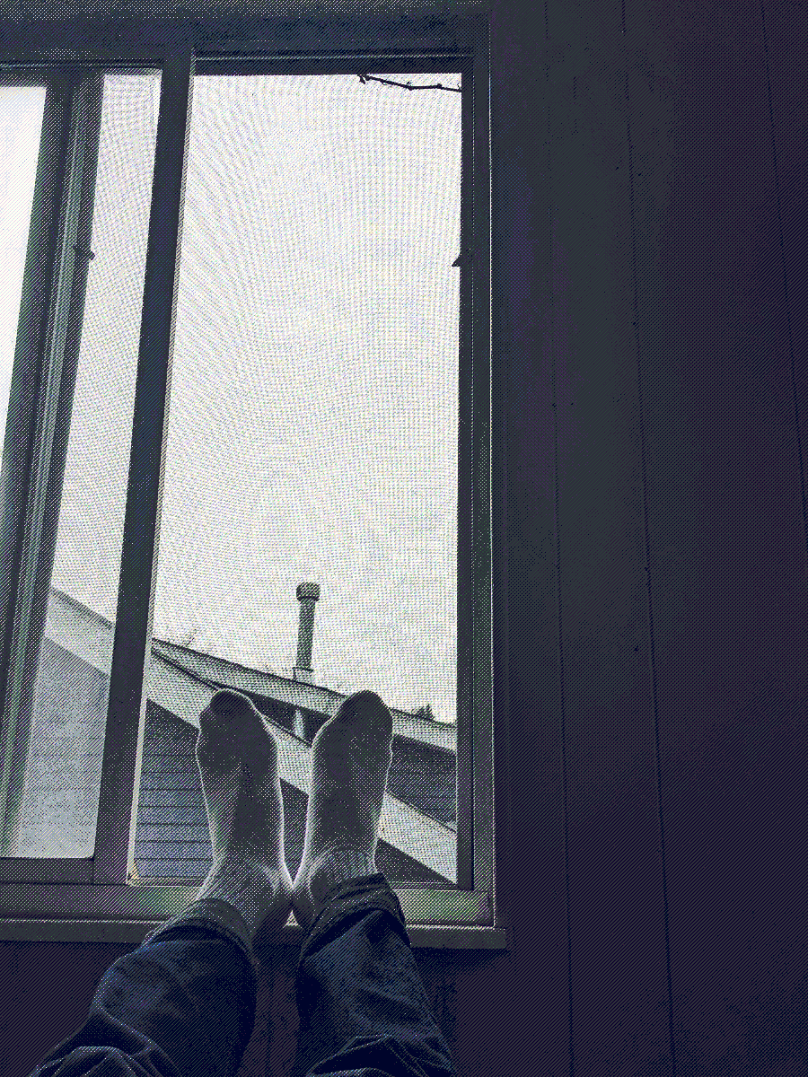 Two feet covered by white socks, elevated and resting on a gloomy windowsill.