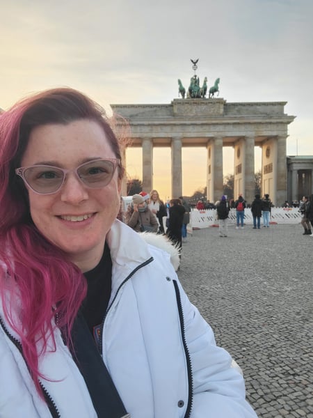Meredith smiles in front of a large neoclassical monument. She is wearing a white winter coat.