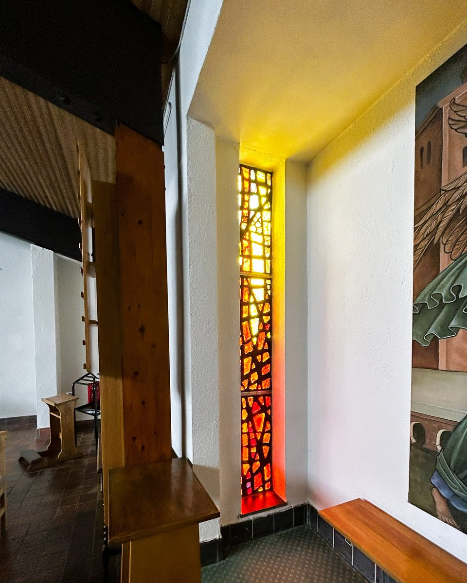 A narrow window, filled with small pieces of glass that shade from yellow at the top to red at the bottom. The white walls of the window embrasure are glowing with the light.