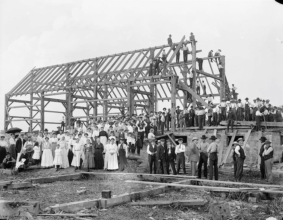 Black and white photo of a large group of people raising a barn.