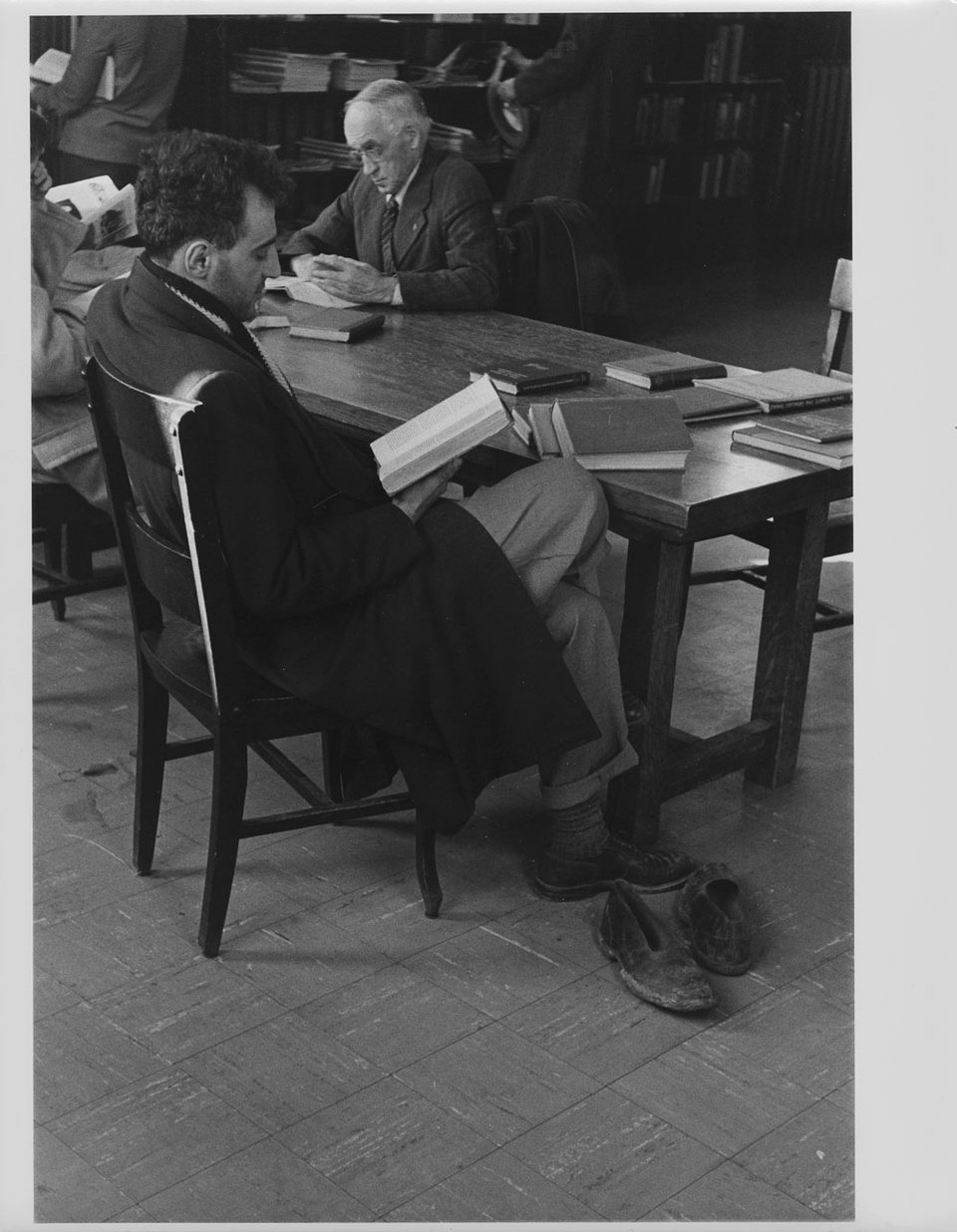 Black and white photo of people seated at a table with books, reading