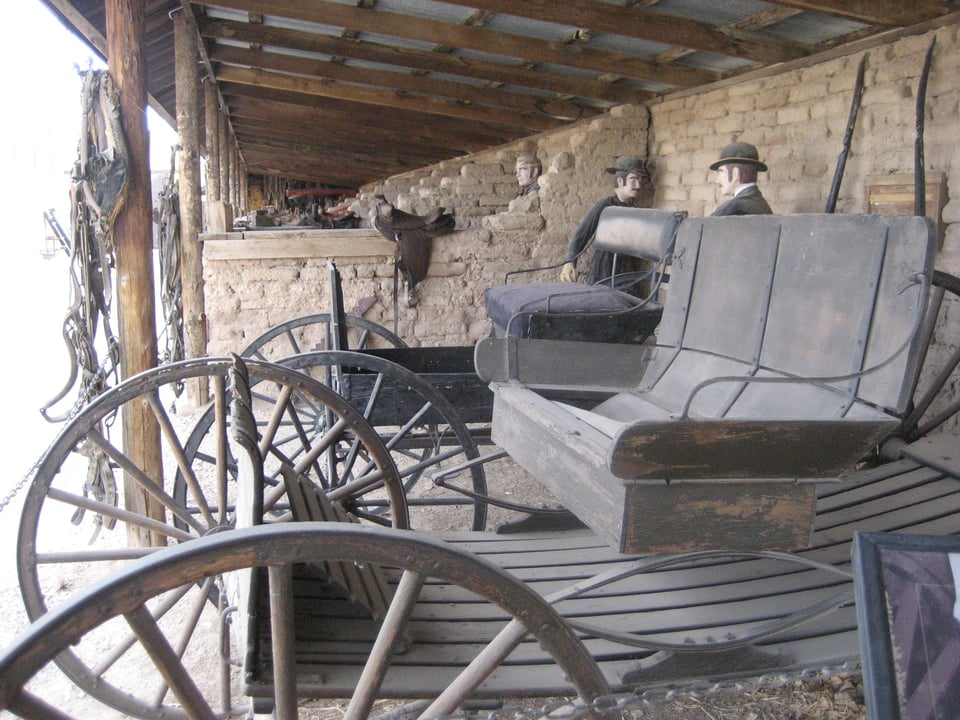 Two old, dusty carriages inside a leanto shed.