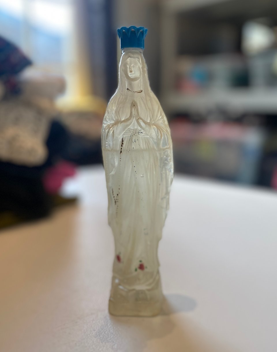 a small clear plastic bottle shaped like Mary and half filled with clear liquid